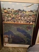 Two framed posters leaning against a wall, one a colorful village scene and the other a vintage map of Italy in a gold frame.