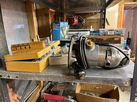 Metal Stanley router on metal shelf with wooden and plastic cases of router bits beside it