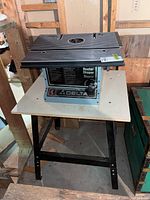 Delta router shaper mounted on a work table in a workshop/basement environment, showing front and side views of the machine and table structure.