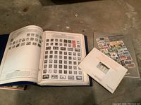 Open world stamp album with black and white vintage stamps and various other stamps alongside the collectors handbook and a sheet of colorful stamps from Commonwealth countries.