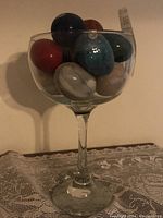 Tall clear glass filled with eight hand carved polished stone eggs of various colors and patterns shown inside the glass