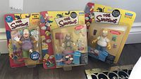 Three Simpsons figurines in original packaging including Krusty the Clown, Itchy and Scratchy, and Homer Simpson