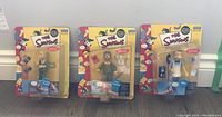 Full view of three Simpsons action figures in original packaging shown side by side