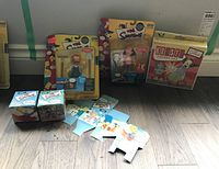 Photo showing three Simpsons action figures in original packaging including Krusty, Bart, and Homer, two Simpsons watches in small boxes, and the Krusty punching doll box along with packaging inserts.