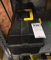 Closed black plastic toolbox with yellow handle and label on top.