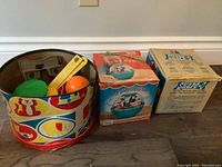 Metal round bin containing various toys, two boxed vintage toys - Fisher-Price Roly Poly Chime Ball and Shape-O toy.
