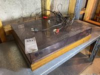 Akai AP 005 turntable closed with its tinted transparent dust cover and RCA cables visible on top, wooden base.