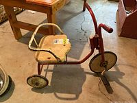 Side angled view of vintage red metal tricycle showing design, white seat, and wheels.