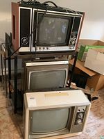 Vintage Sony TV on top of a metal rack with two other TVs below, showing wood paneling and control knobs