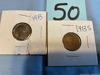 Two early Lincoln pennies from 1913 and 1913-S in cardboard holders, shown on a blue surface.
