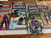 Photo showing a variety of 14 comic books including Justice League of America, Realm of Kings: Nova, multiple Superman issues, and The Punisher 2099 titles laid out on a table.