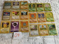 Photo of all 18 Pokemon cards laid out in three rows on a white lace tablecloth.