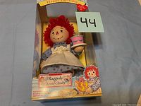 Photo showing Raggedy Ann doll in original box holding birthday cake, front view