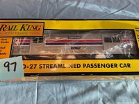 Close-up of Rail King O-27 Streamlined Passenger Car in original yellow box with clear window showing car body and paint details