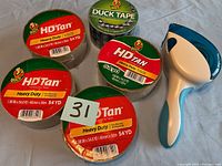 Five rolls of tape and one tape dispenser displayed on a flat surface, showing brand labels and tape dimensions.
