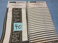 Photo showing two sets of 3 pack kitchen towels, one with text design and the other with gray and white stripes, new with labels from Kitchen Collection.