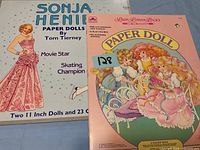 Photo of Sonja Henie Paper Dolls box and Lacy Lover's Locks Paper Doll book showing cover art and titles