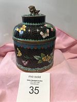 Front view of floral and bird decorated cloisonné jar with lid featuring foo dog finial