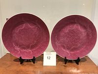 Two deep pink Asian dragon motif ceramic plates placed on display stands on a wooden surface.