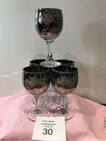 Set of five dark tinted wine glasses with etched floral designs displayed on a pink cloth background.