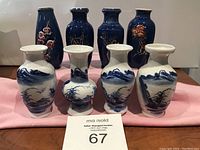 Set of 8 small Asian-style vases, with four white porcelain vases painted in blue landscapes in front and four taller dark blue vases with floral and bamboo motifs behind, arranged on a table for display.