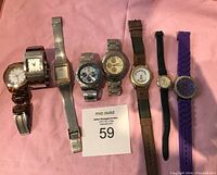 Overview image of 8 assorted watches laid on pink fabric, showing variety in band materials and dial designs