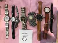 Photo of eight assorted watches laid out on pink fabric, showing front faces and bands.