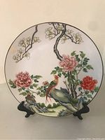 Front view of the round porcelain plate showing the fully painted birds, flowers, and tree branch design.