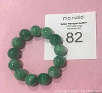 Photo showing round green jade beads strung to form a bracelet on a pink surface.