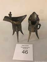 Two Asian bronze liquor vessels displayed together showing shape, legs, and engraving.