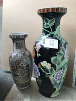Photo showing two Asian decorative vases side by side, one with white background and painted traditional scenes, the other black with large floral patterns