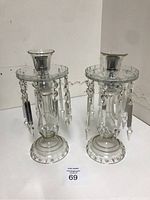 Pair of clear crystal glass candlesticks with hanging prism decorations on a white surface.