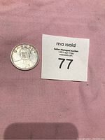 Silver coin on pink fabric next to an auction label, showing the embossed portrait of Dr. Sun Yat-sen and some Chinese characters.