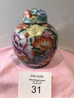 Front view of a colorful floral porcelain ginger jar with lid on pink cloth background.