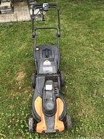 Front view of the WORX lawn mower on grass, showing handle, motor housing, and wheels