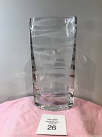 Full front view of clear Marcaurel glass vase with etched wave pattern on a pink cloth background.