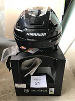 Front view of the black Warrior Alpha One Pro hockey helmet placed on top of its original box showing the brand logo and product name.