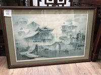 Framed painting shows a misty depiction of traditional Asian buildings with water and bridges, framed under glass