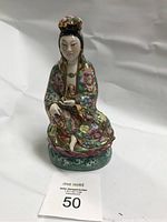 Front view of porcelain figurine showing detailed painted floral robe and seated woman holding small object.