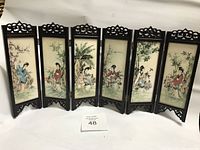 Full view of small six-panel folding screen with porcelain painted panels depicting Asian women and nature scenes, framed in dark carved wood.