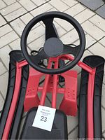 Top view of red and black snow sled showing steering wheel, seat, and frame detail.