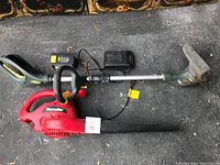 Full view of leaf blower, string trimmer, rechargeable battery, and battery charger on pavement.