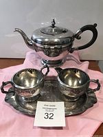 Silver plated teapot, creamer, and sugar bowl on the tray photographed with a pink cloth background and auction lot card