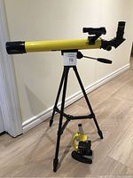 Yellow telescope mounted on a black tripod with microscope placed on floor next to it.
