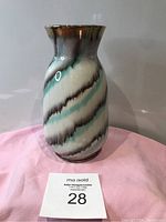 Front view of the ceramic vase with turquoise, brown, and white swirling stripes on a pink cloth background.
