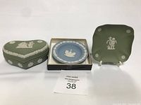 Group photo of Wedgwood jasperware items: green heart-shaped container with lid, blue round plate in box, green square plate on stand
