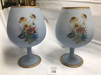 Two light blue frosted wine glasses with colorful floral designs and gold rims and bases.
