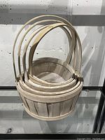 Five nested wooden baskets made of light wood with rounded handles, shown stacked inside each other for size comparison.