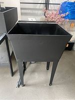 Black utility sink standing on four legs, shown empty.