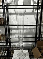 Single clear glass trumpet vase on shelf with flared opening, stem, and round base.